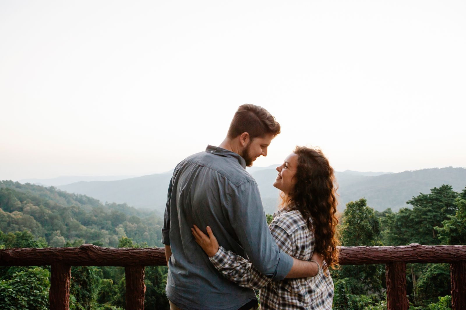 A couple on a teak balcony above forested hills