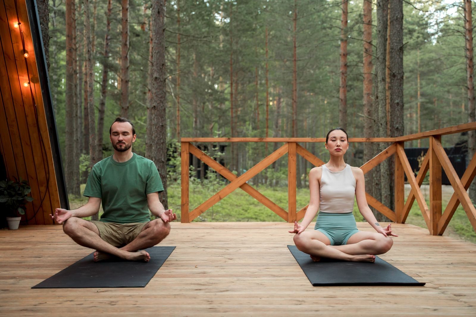 Two people meditating side by side on a deck in the trees