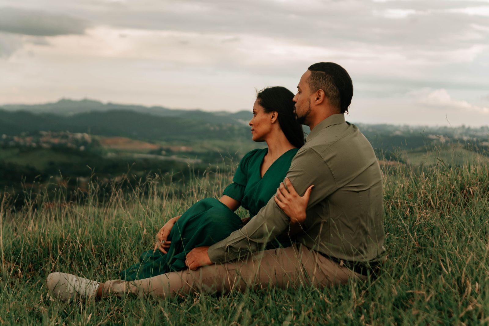 A couple sitting close on a hillside, looking out