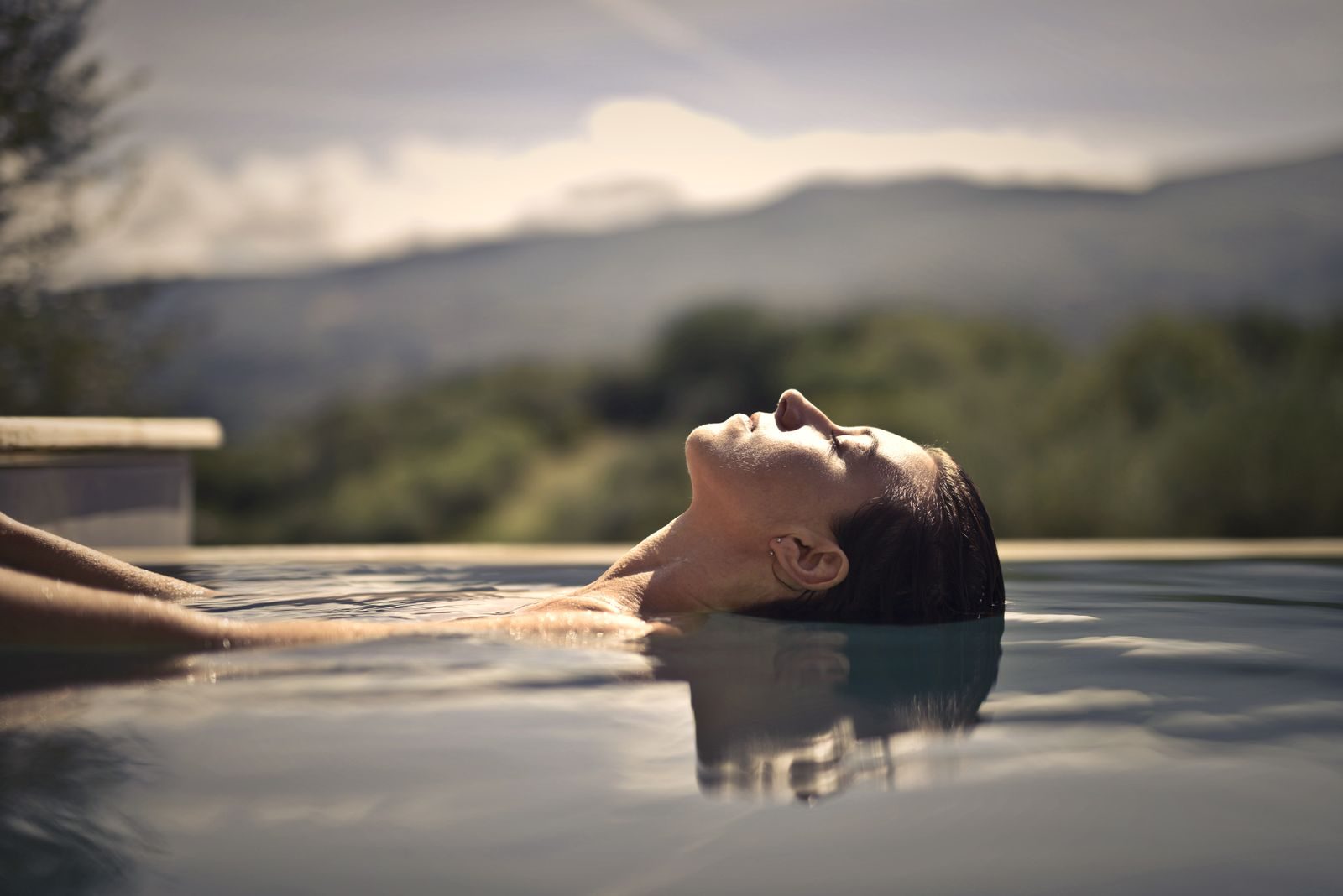 Floating in an infinity pool, eyes closed, hills behind
