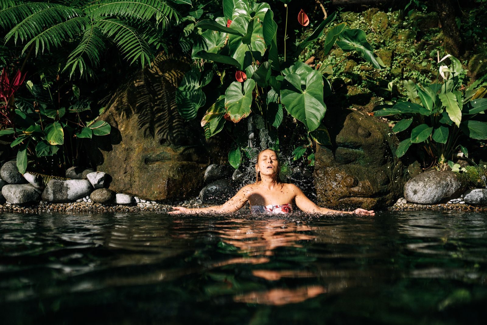 A woman in a natural pool under tropical plants