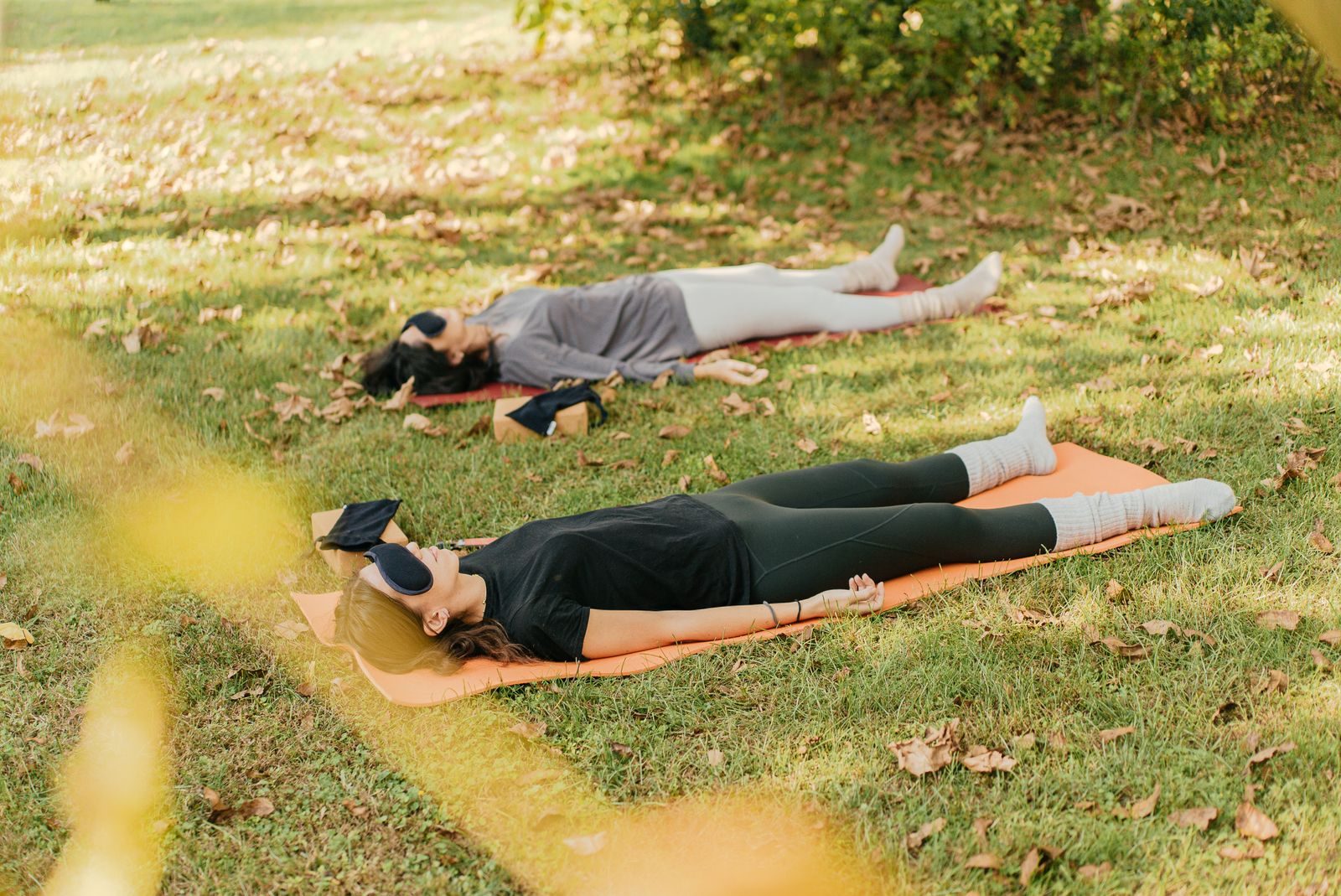 Two people lying on mats on the grass, eye masks on