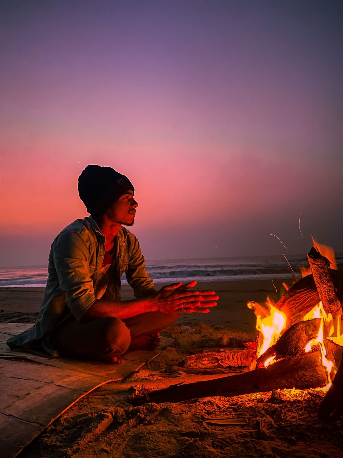A figure warming his hands at a fire at dusk