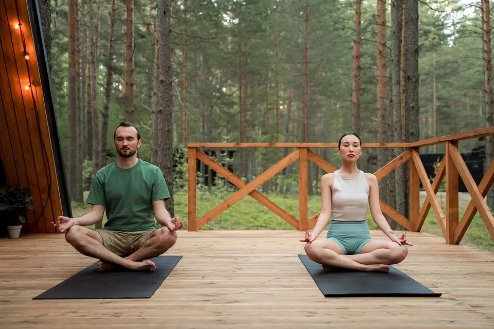 Two people meditating side by side on a deck in the trees