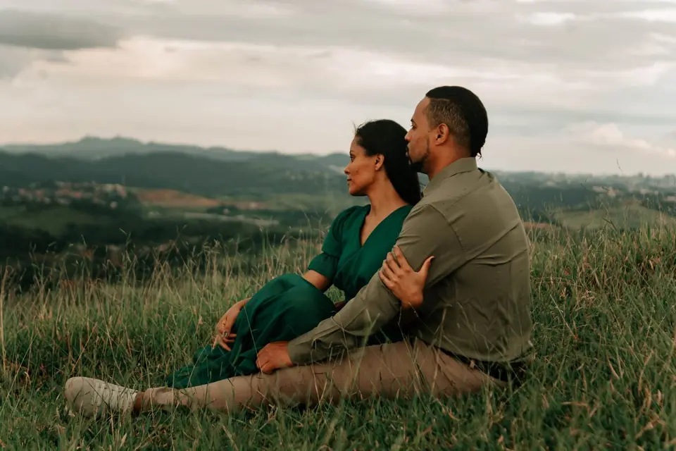 A couple sitting close on a hillside, looking out