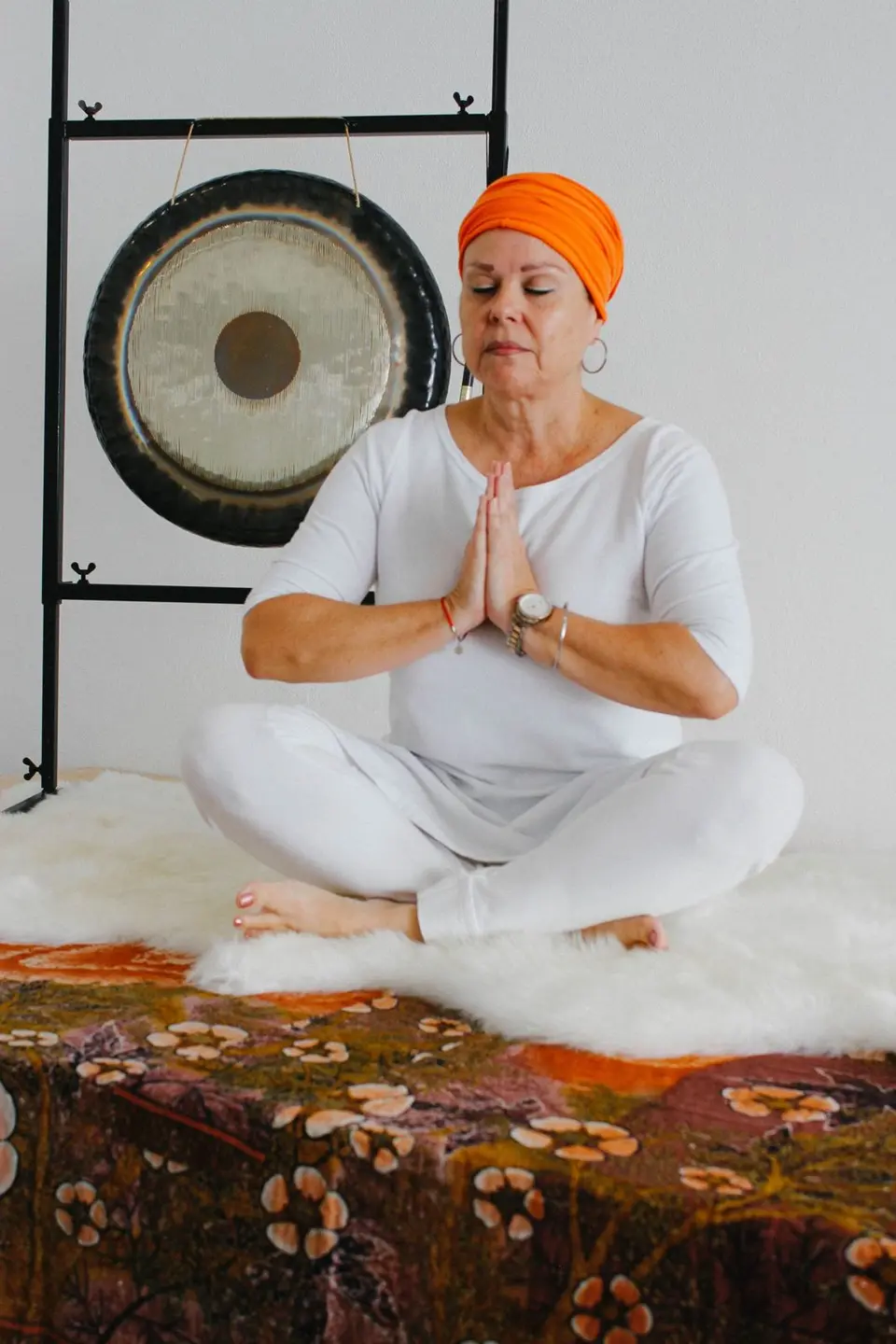 A woman in white, hands at the heart, a gong behind her
